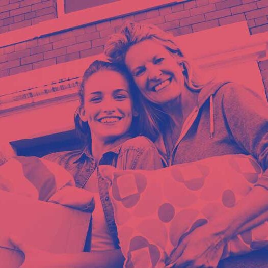 young adult with an older adult holding a pillow, teddy bear and moving boxes