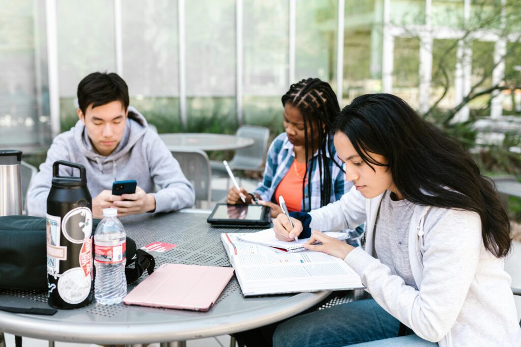 Three young adult students studying on an outdoor table