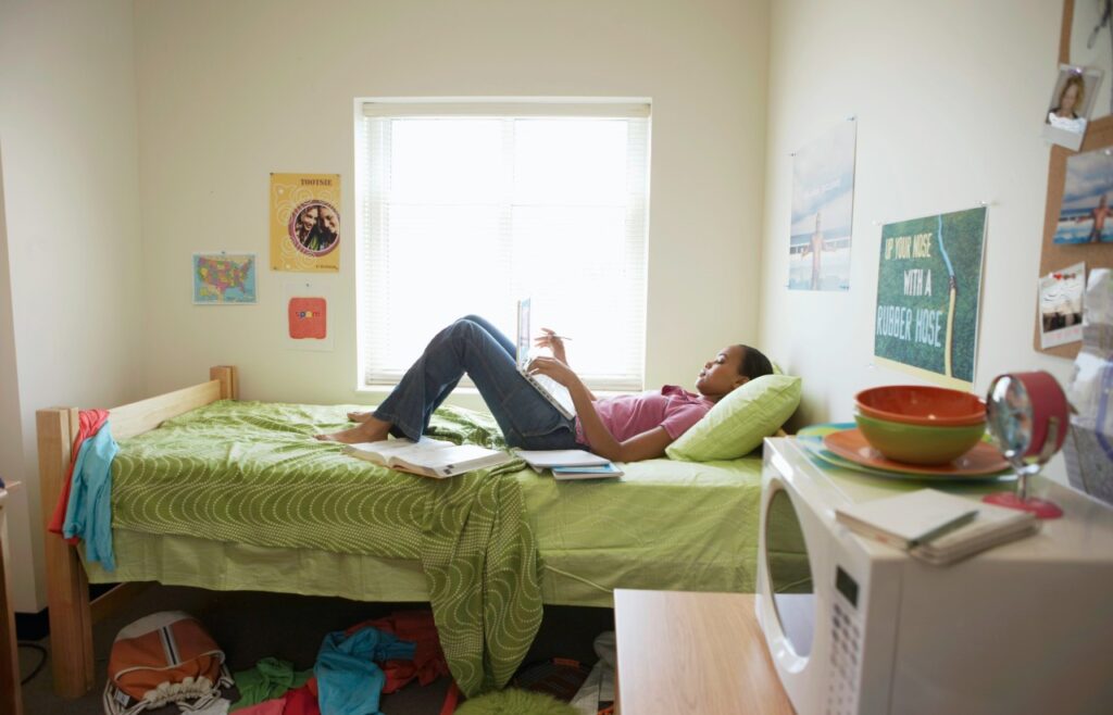 young woman laying on a bed in a university student dorm room