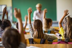 Children putting their hands up to answer question for the teacher.