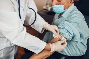 Doctor putting a plaster on an older man after vaccination